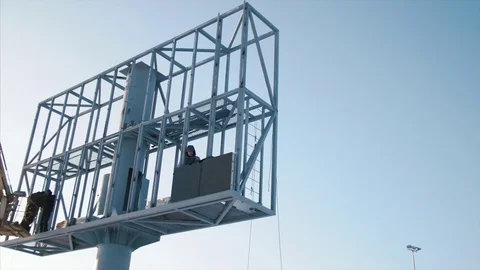 Worker in lift bucket during installation big billboard in bad weather. Workers Stock Footage 84743431