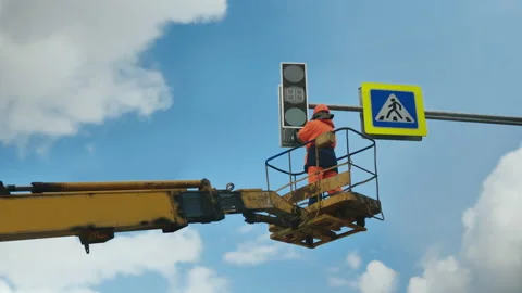A worker in a lift cradle repairs an LED traffic light. LED technology. Stock-Footage 140109853