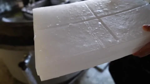 Worker lifting a large solidified white wax block from a cooling water tank at Stock Footage 343875847