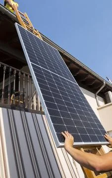 Worker lifting solar panel up ladder to rooftop. Stock Photos