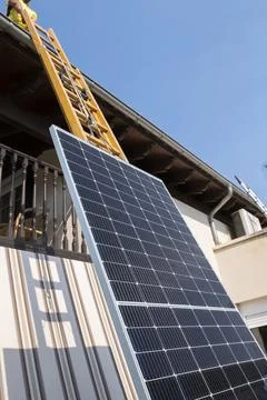 Worker lifting solar panel up ladder to rooftop. Stock Photos