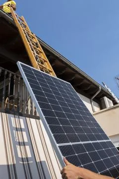 Worker lifting solar panel up ladder to rooftop. Stock Photos