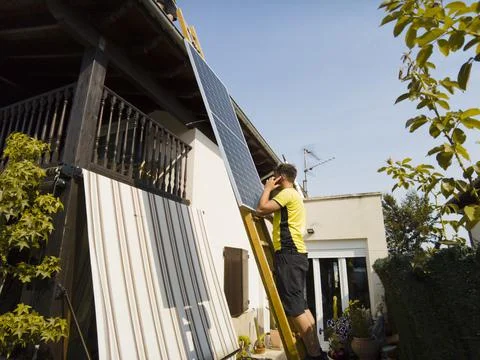 Worker lifting solar panel up ladder to rooftop. Stock Photos