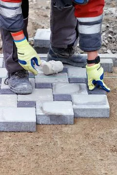 A worker in light green work gloves is laying paving slabs under the level of Stock Photos