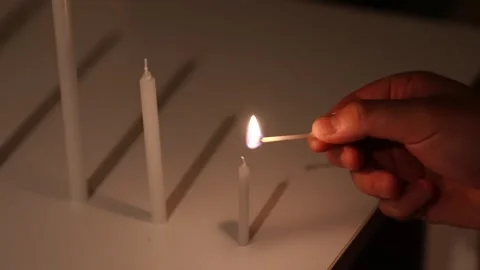 Worker lighting a small candle with a match beside a taller unlit candle on a Stock Footage 343875974