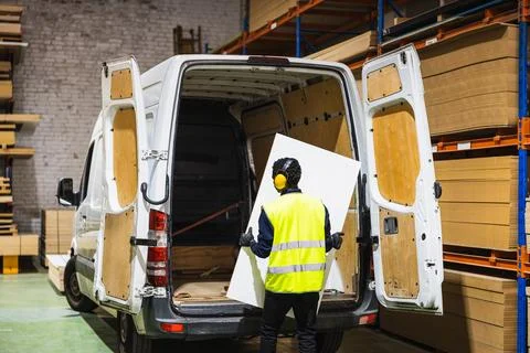 Worker loading wood panel into delivery van Stock Photos