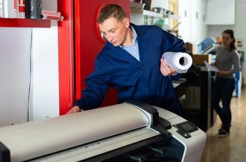 Worker loads new roll of paper into the plotter Foto stock