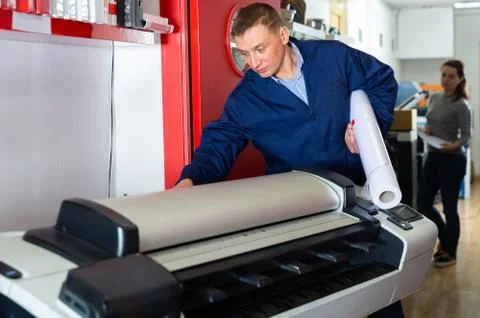 Worker loads new roll of paper into the plotter Stock Photos