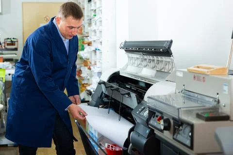 Worker loads new roll of paper into the plotter Stock Photos