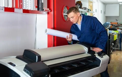 Worker loads new roll of paper into the plotter Stock Photos