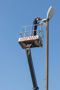 Worker Maintains Streetlight From Elevated Platform Under Clear Sky Stock Photos