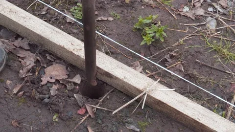 A worker makes a hole in the ground with a crowbar to install a fence post. Stock Footage 157286967