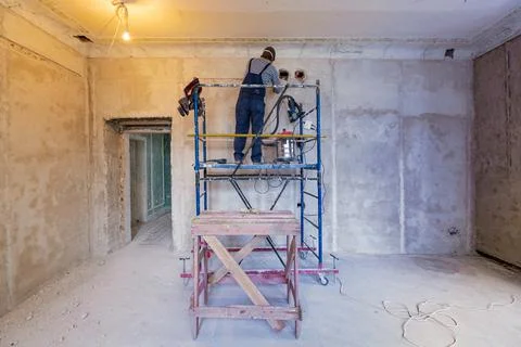 Worker is making a technological hole for electrical cabel in the wall in Stock Photos