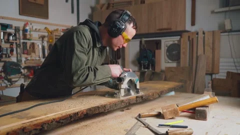 Worker male builder works in a workshop, cuts a board with a circular saw in Stock Footage 241075613