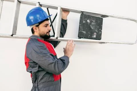 Worker man with beard carries a ladder on his shoulder on white background Stock Photos