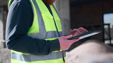 Worker man hands hold tablet computer at construction site in safety vest Stock Footage 274481136
