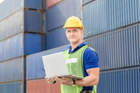 Worker man in hard hat and safety vest holding laptop, Foreman control loadin Fotos de archivo