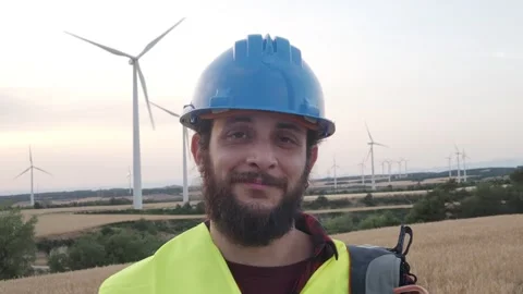 Worker man with helmet looking at camera smiling in a field of windmills Stock Footage 245114127