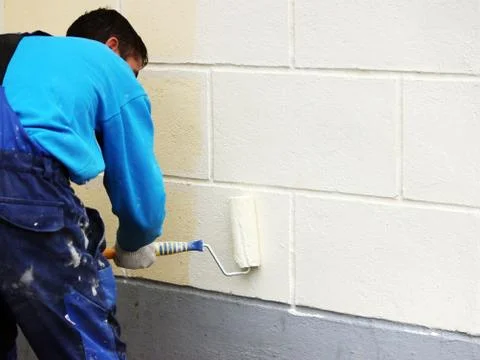 Worker man painter paints the wall with beige paint  a roller. Stock Photos