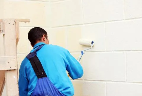 Worker man painter paints the wall with beige paint  a roller. Stock Photos