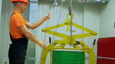 Worker manages barrels in warehouse using chain hoist, ensuring organized Stock Footage 281934742