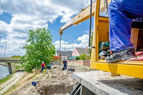 Worker is managing mobile crane and pulling huge pipe in the trench Stock Photos