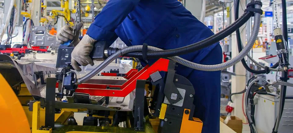 Worker maneuvers a precision tool on an assembly line in a modern manufactu.. Stock Photos
