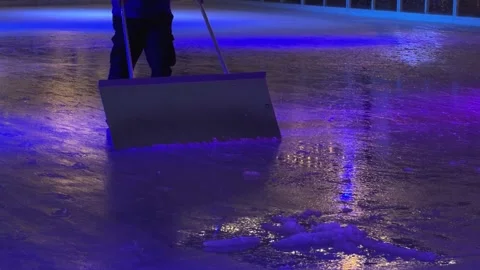 Worker manually cleaning an ice rink surface with a large scraper, reflecting Stock Footage 345665645