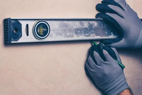 A worker marks a hole for drilling the attachment of the hanging shelf. Stock Photos