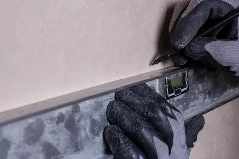 A worker marks a hole for drilling the attachment of the hanging shelf. Stock Photos