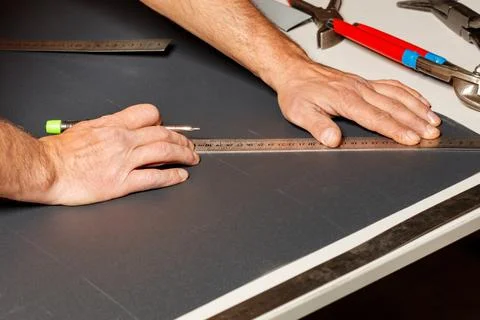 A worker marks out a sheet of roofing iron with a pencil and a ruler. Stock Photos