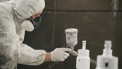 A worker in a mask and uniform paints a metal pipe at the factory Stock Footage 234476703