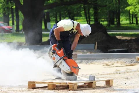 A worker mason cuts a curb with a circular saw when building a parking lot for Stock Photos