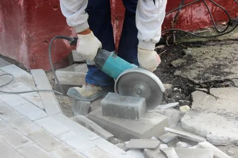 A worker mason cuts a curb with a circular saw when repair of the sidewalk Stock Photos