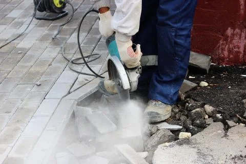 A worker mason cuts a curb with a circular saw when repair of the sidewalk Stock Photos