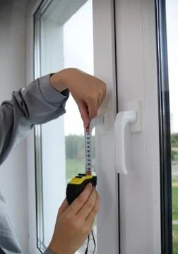 A worker measures the handles of the window frame with a tape measure. Stock Photos
