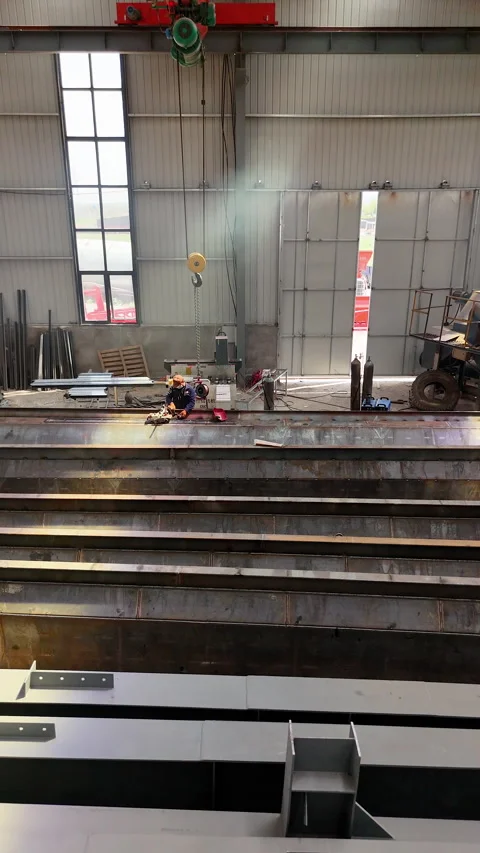 A worker measures a metal beam in a large metal fabrication plant to begin  Stock Footage 335793408
