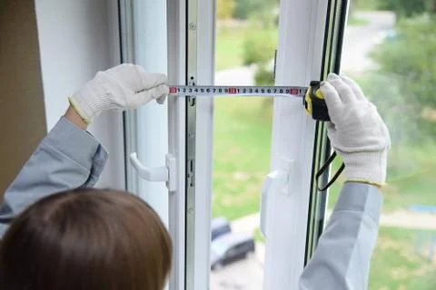 A worker measures an open window frame with a ruler. Stock Photos