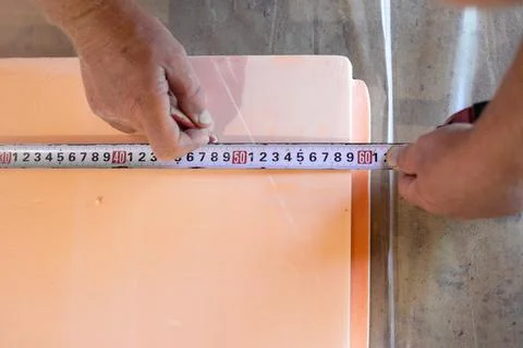 A worker measures polystyrene foam for laying on the floor. Insulation of t.. Stock Photos