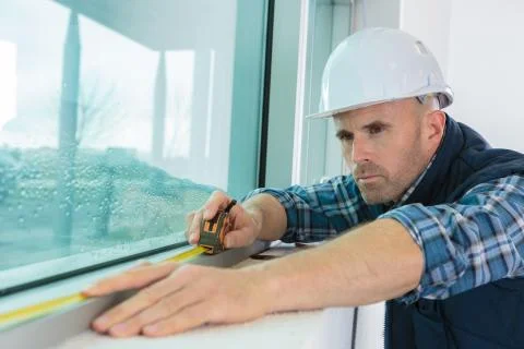 Worker measuring a window at construction site Stock Photos