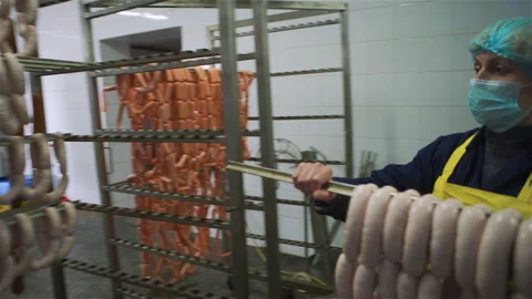 Worker in meat factory hangs raw sausage on metal sticks for further baking. Vídeo Stock 131865065