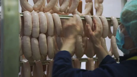 Worker in meat factory hangs raw sausage on metal sticks for further baking. 库存影片 131865286