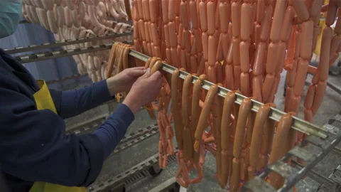 Worker in meat factory hangs raw sausage on metal sticks for further baking. Vídeos de archivo 131870264