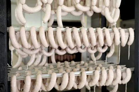 A worker at the meat processing factory, prepares sausages at the work table Stock Photos