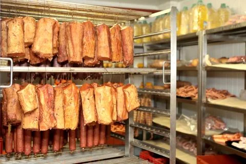 A worker at the meat processing factory, prepares sausages at the work table Stock Photos