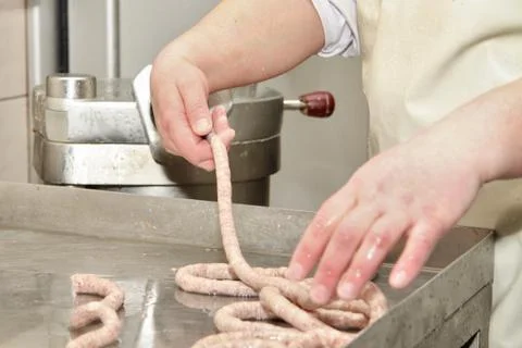A worker at the meat processing factory, prepares sausages at the work table Stock Photos