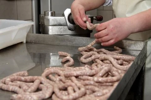 A worker at the meat processing factory, prepares sausages at the work table Stock Photos