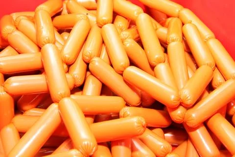 A worker at the meat processing factory, prepares sausages at the work table Stock Photos