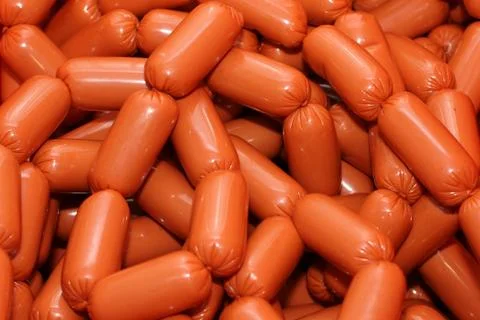 A worker at the meat processing factory, prepares sausages at the work table Stock Photos