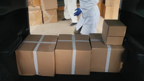 Worker in medical coat unloading cardboard boxes from car trunk for medical.. Stock Footage 334605505